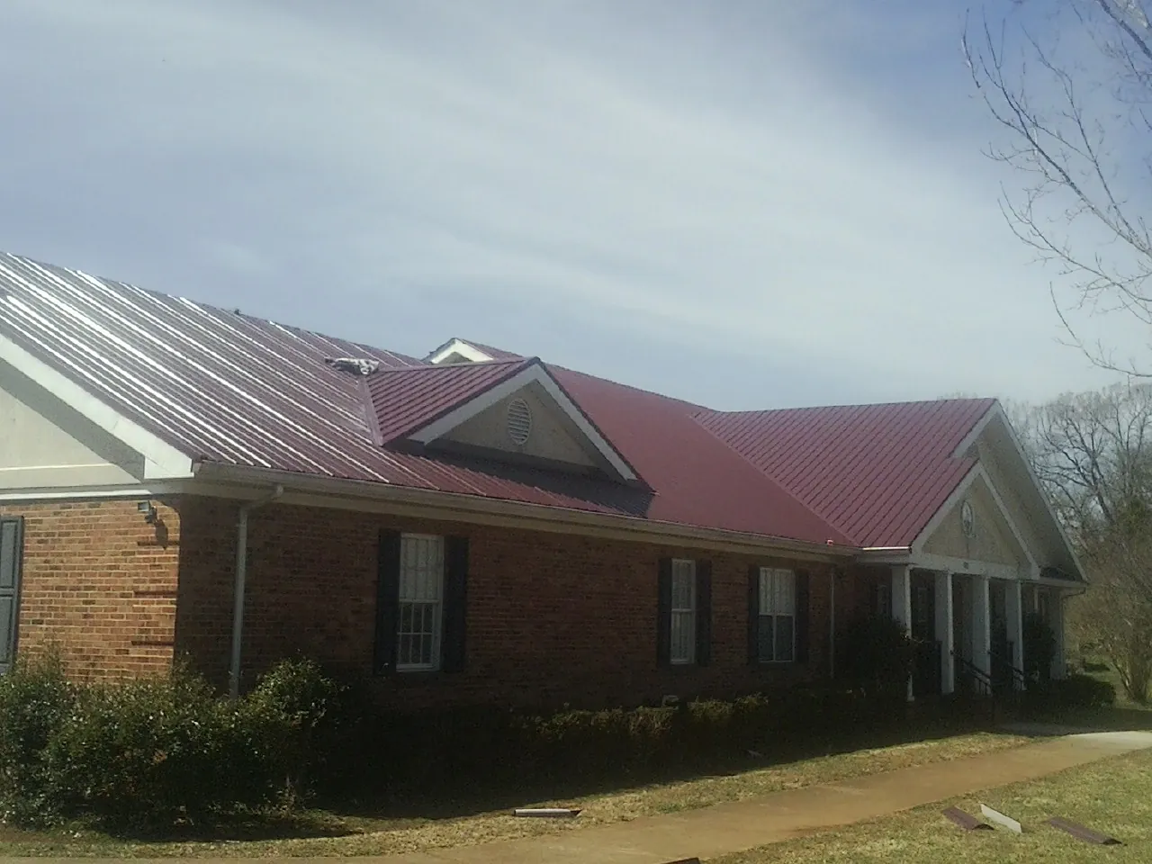 Red metal roof with gabled entries on a long brick building, from a Hail Damage Roof Repair job in Callaway