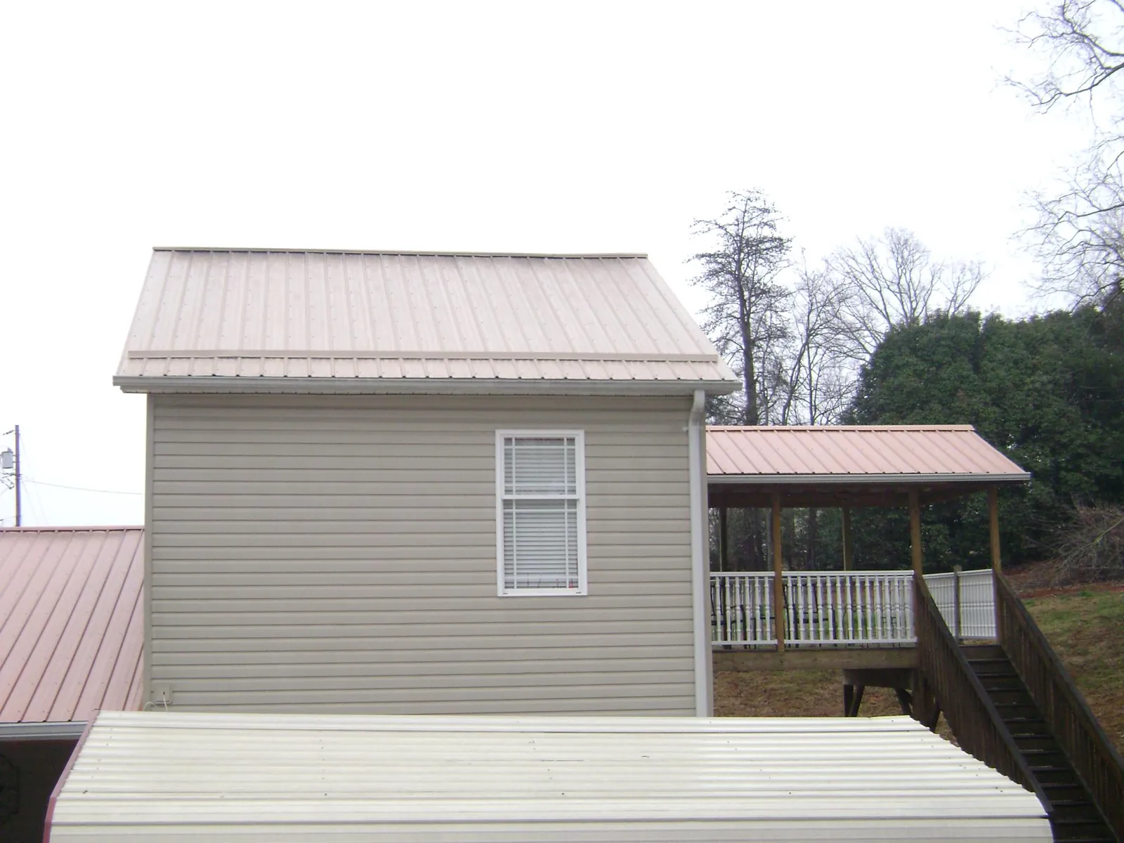 Tan metal roofs on a two story addition and attached porch, from a Roof Replacement job in Callaway